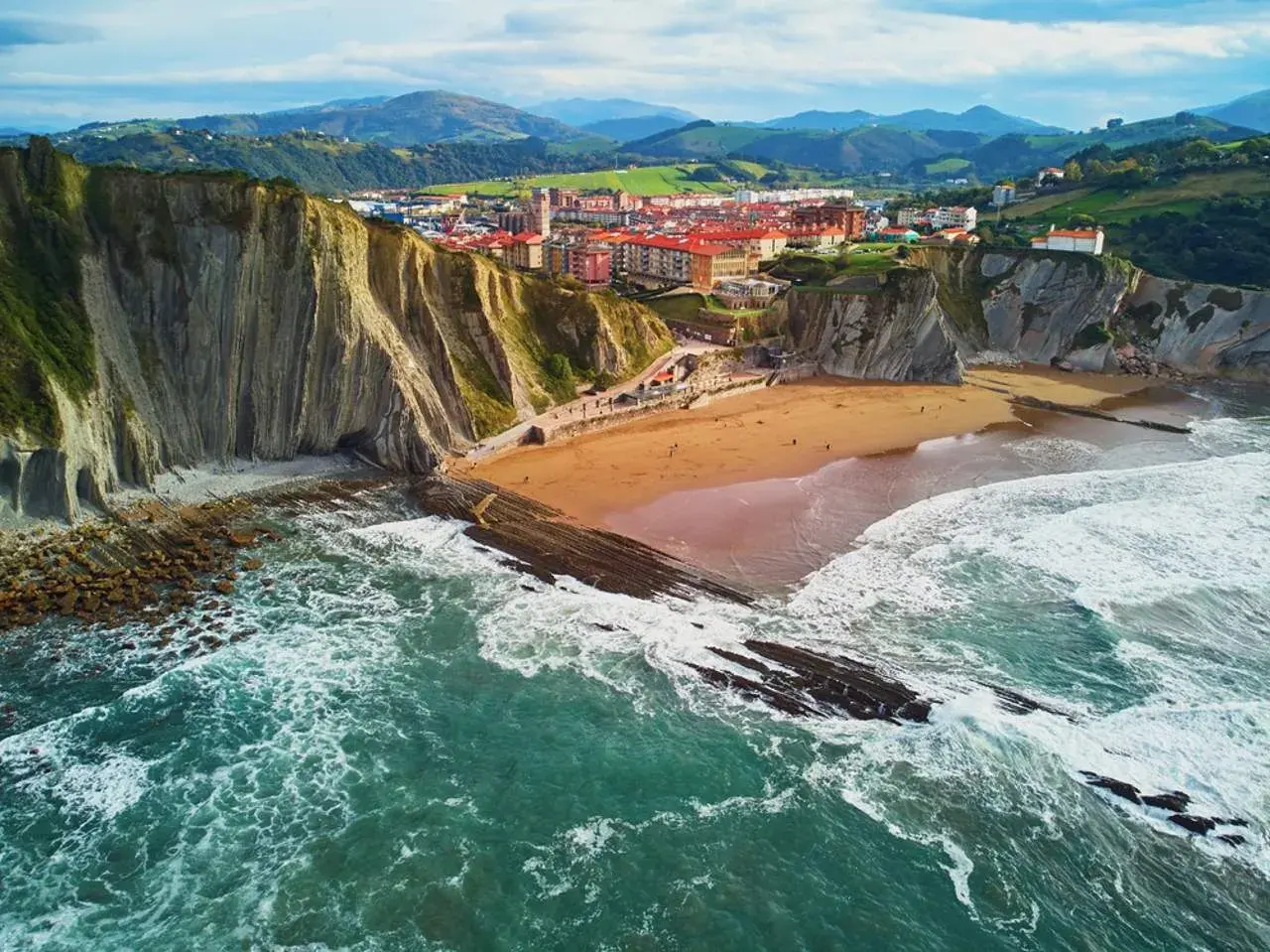 Impresionantes paisajes del País Vasco: acantilados, playa dorada y el mar Cantábrico rompiendo en rocas.