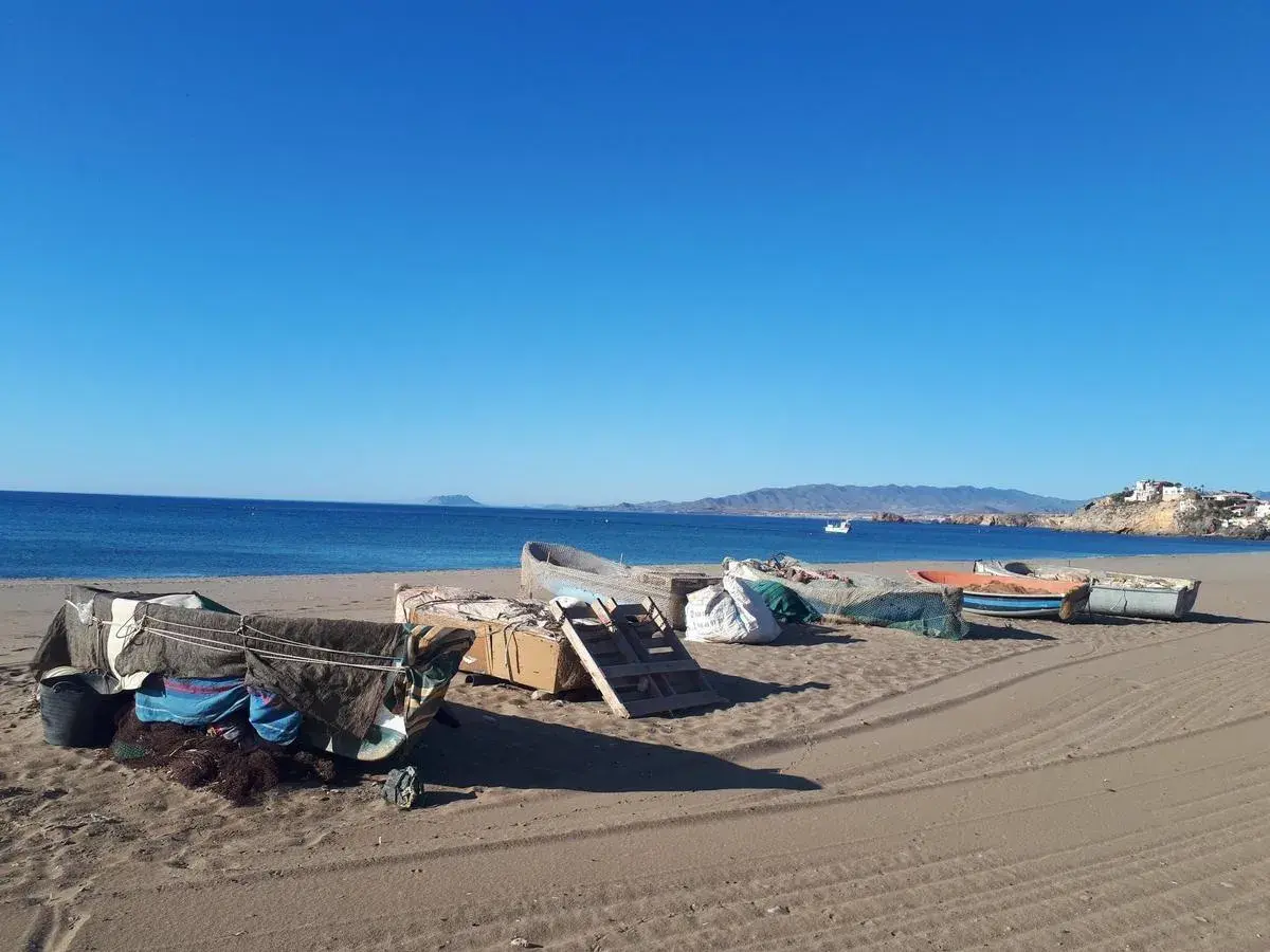 Barcas de pesca cubiertas en la arena de las playas de Mazarrón, con el mar azul y montañas al fondo.