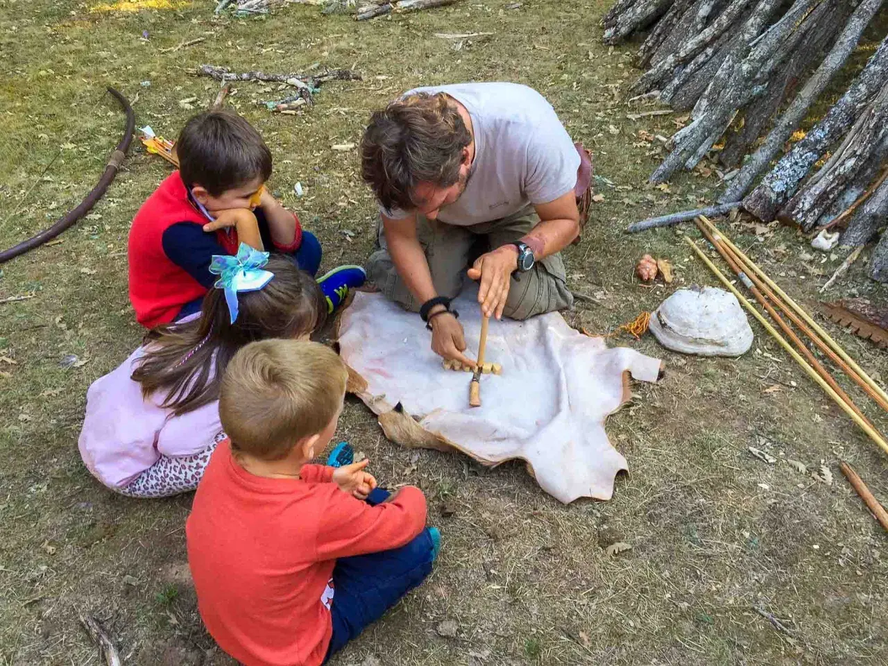 Un hombre enseña a niños a hacer fuego con un arco y un trozo de cuero. ¡Una aventura en la naturaleza para los más pequeños!