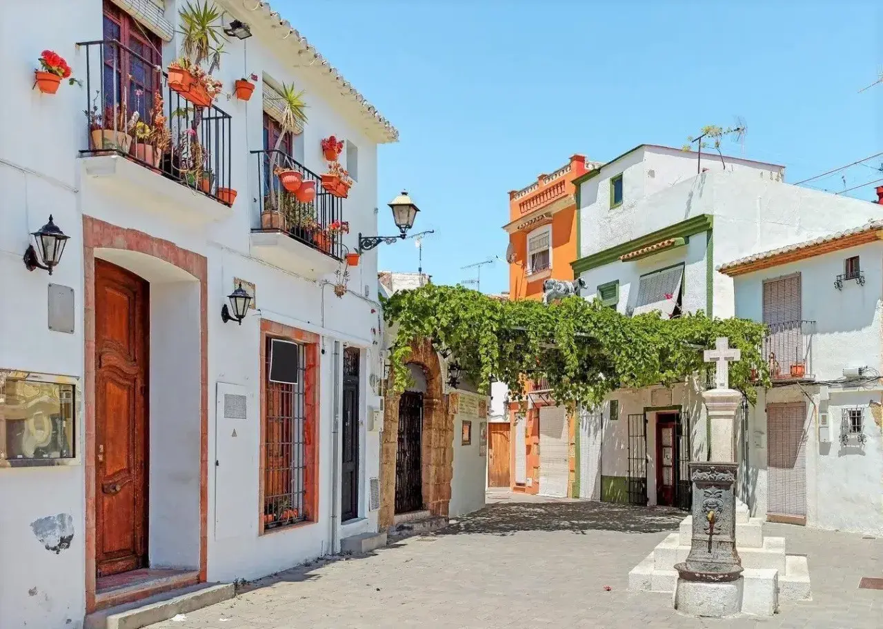 Callejuela con casas blancas, balcones floridos y una fuente. Así es donde está Denia, un rincón con encanto.