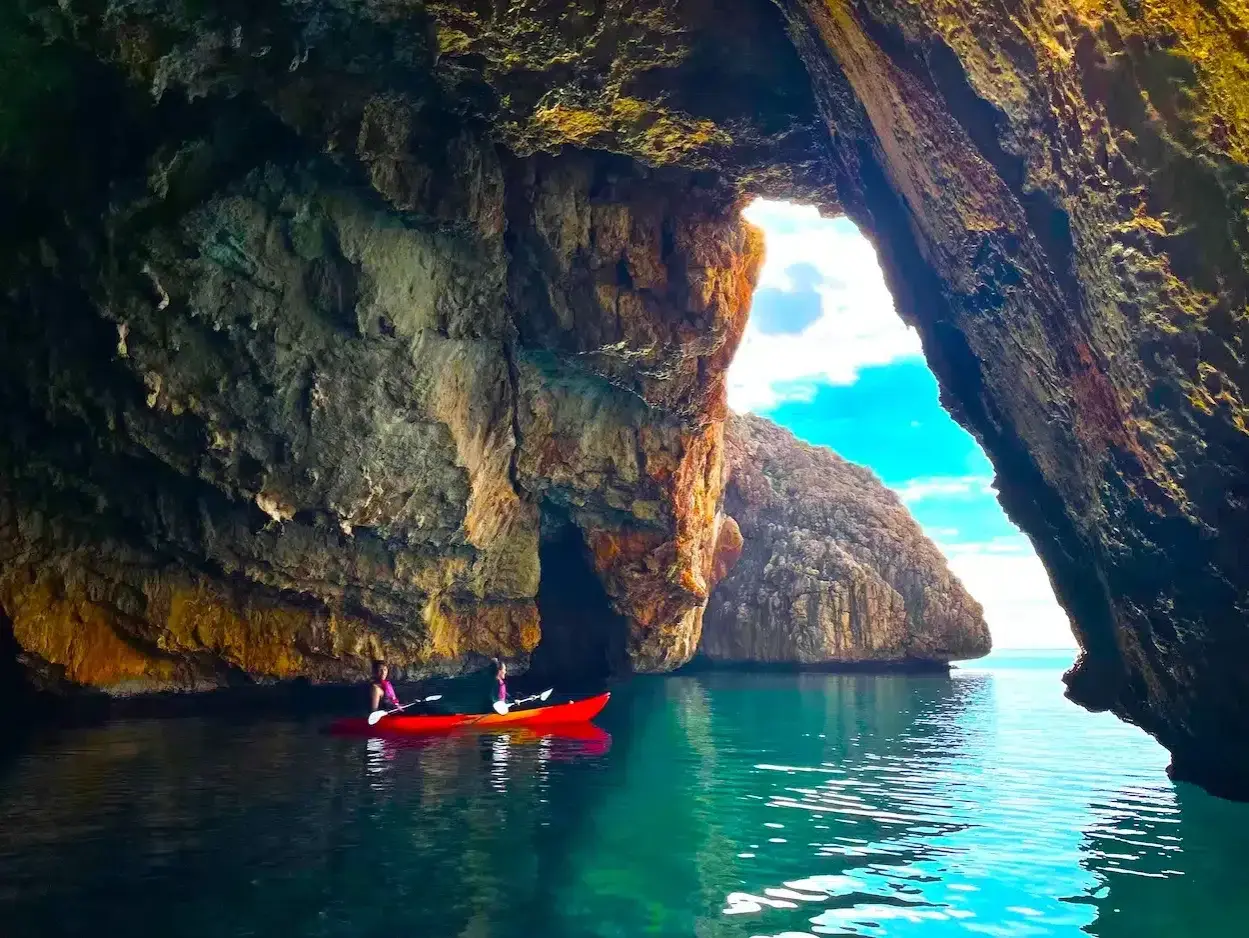 Dos personas en kayak exploran la Cova del Llop Mari en Jávea, con aguas turquesas y formaciones rocosas impresionantes.
