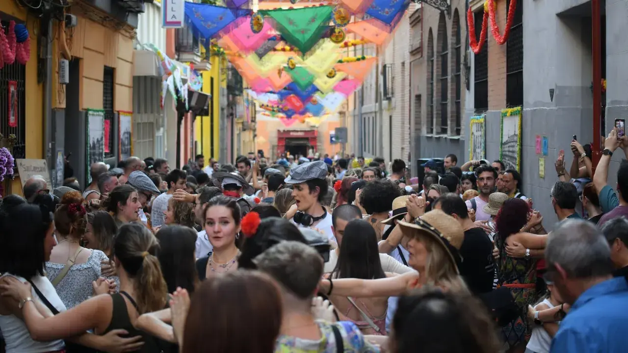 Gente bailando en las fiestas San Cayetano Madrid, con coloridas telas adornando la calle.