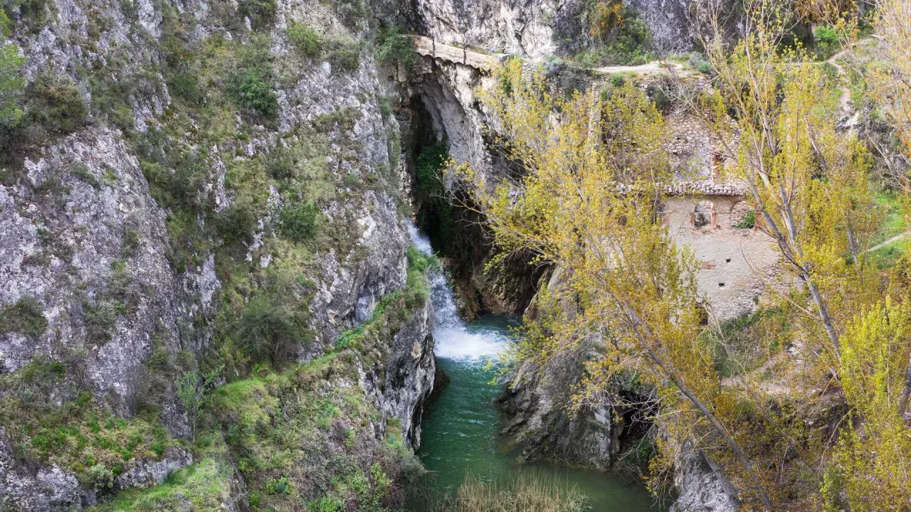 Cascada y ruinas en un cañón. Para saber benilloba como llegar, sigue el sendero entre las rocas y la vegetación otoñal.