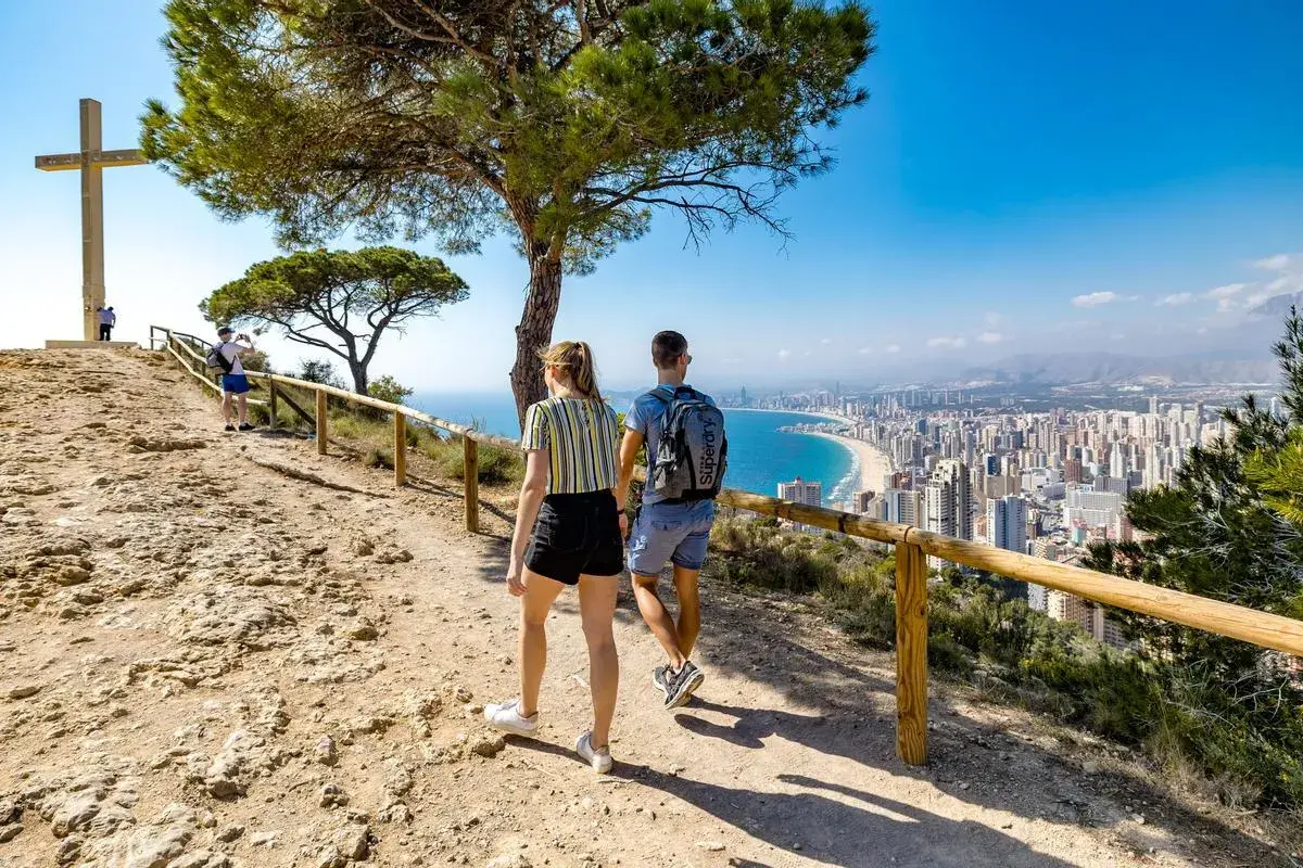Pareja camina hacia la Cruz de Benidorm, con vistas a la ciudad y la playa.