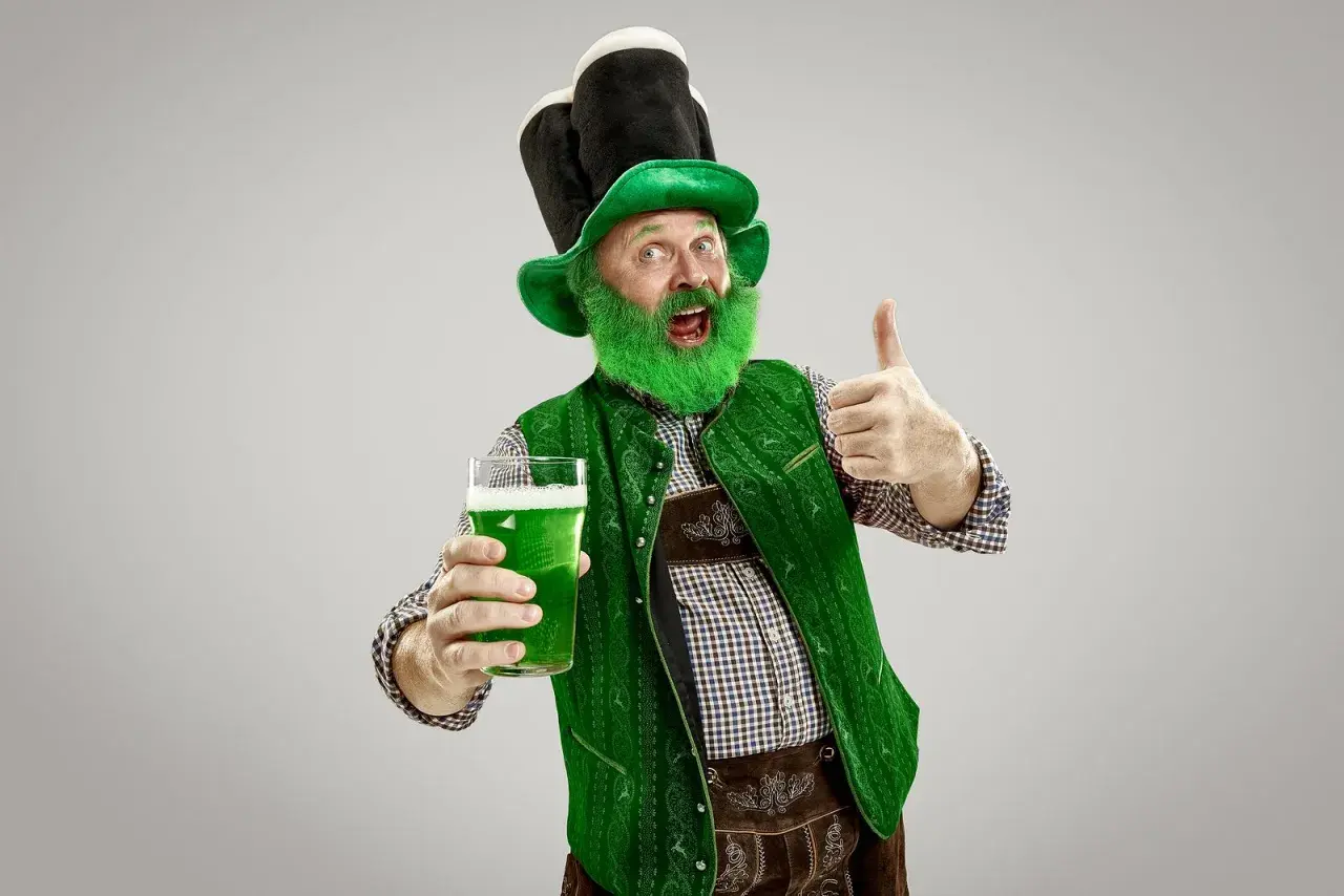 Hombre con barba verde y sombrero de duende, sosteniendo una cerveza verde y dando pulgar arriba. ¡Listo para el desfile de San Patricio!