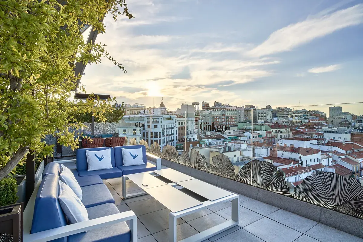 Terraza del Ginkgo restaurante & sky bar con vistas a la ciudad al atardecer. Sofás azules y mesa de centro.