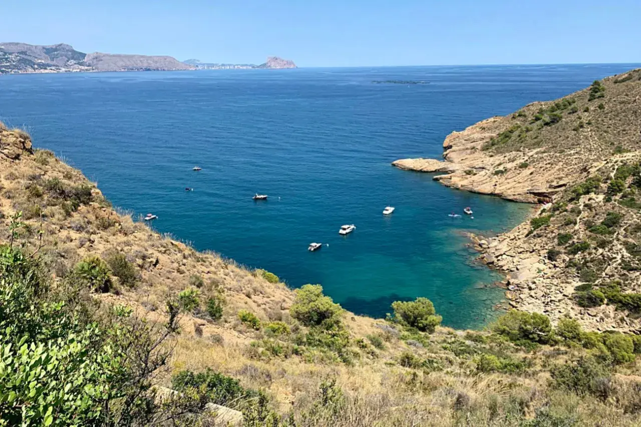 Vista panorámica de la cala de la mina, con aguas turquesas y barcos navegando.