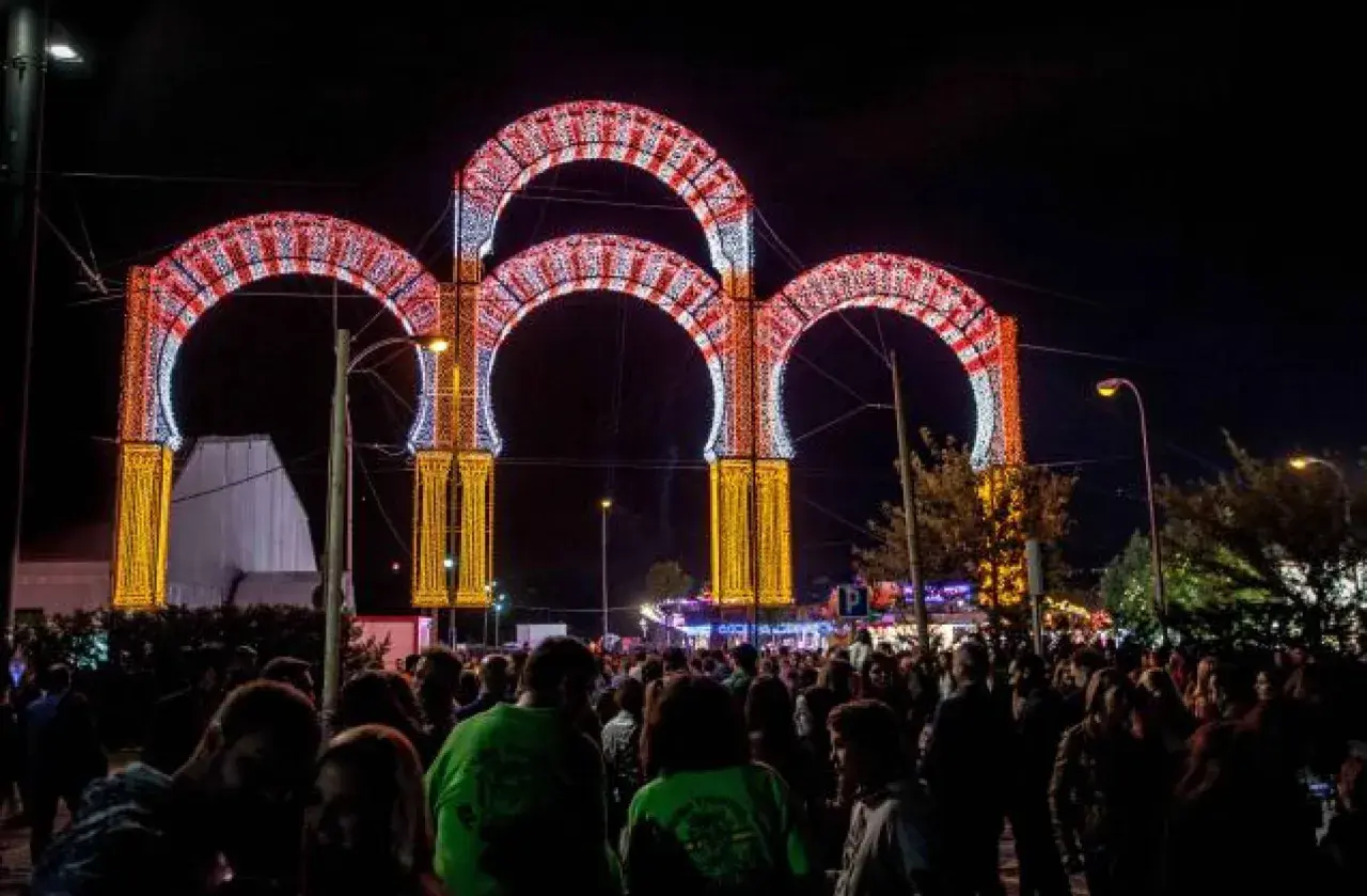 Noche de luces y alegría en las fiestas de Boadilla del Monte. Arcos luminosos decoran la entrada a un evento multitudinario.