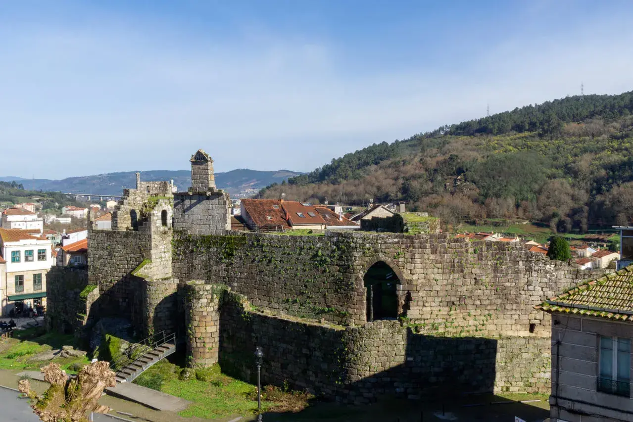 Ruinas de un castillo de piedra, con tejados rojos y colinas verdes al fondo. Un ejemplo de los pueblos bonitos cerca de Monforte de Lemos.