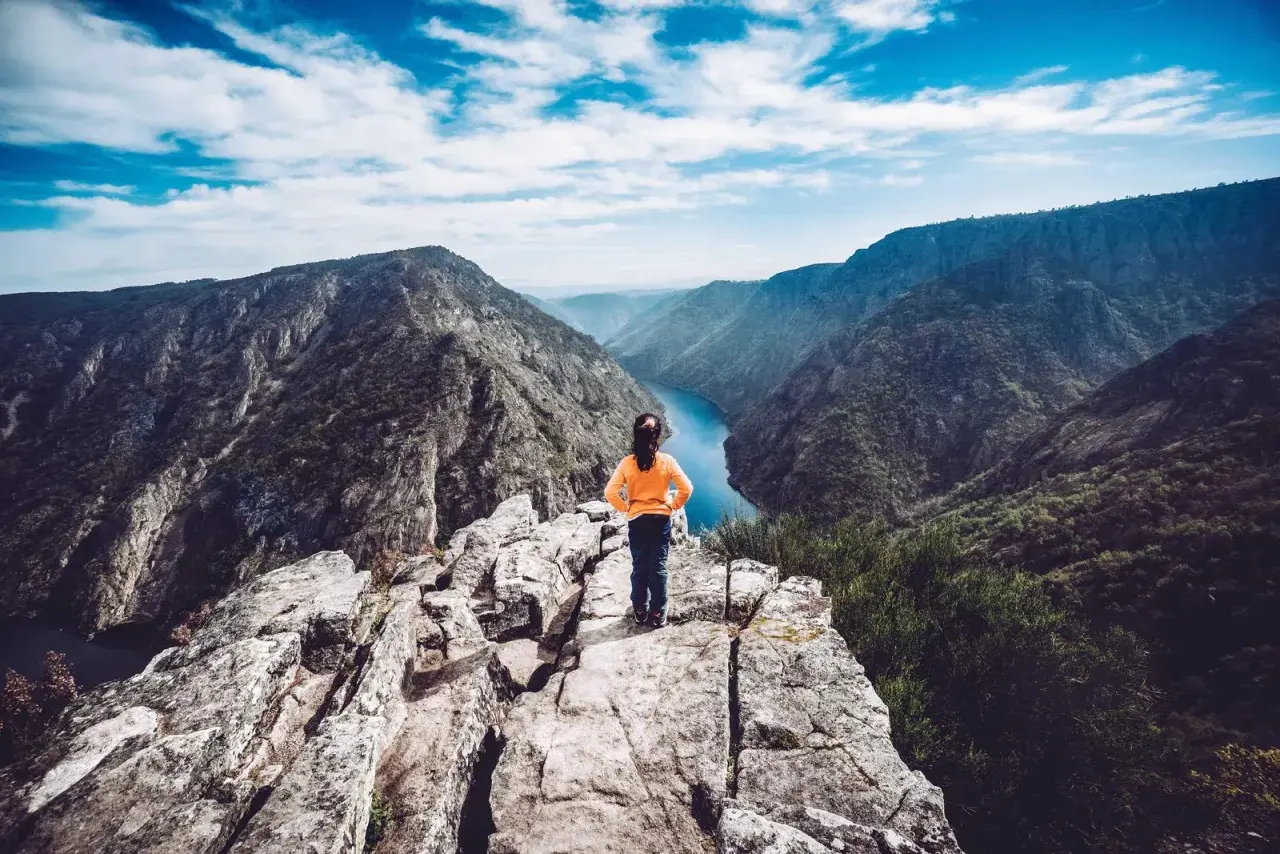 Niña en el mirador de Vilouxe, contemplando un cañón con un río azul y montañas verdes bajo un cielo nublado.