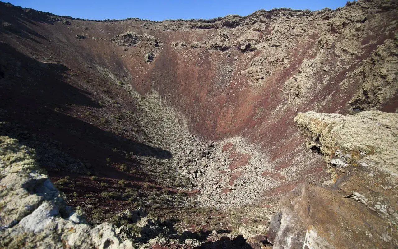 Interior del cráter del Volcán de la Corona, con rocas rojizas y vegetación escasa.
