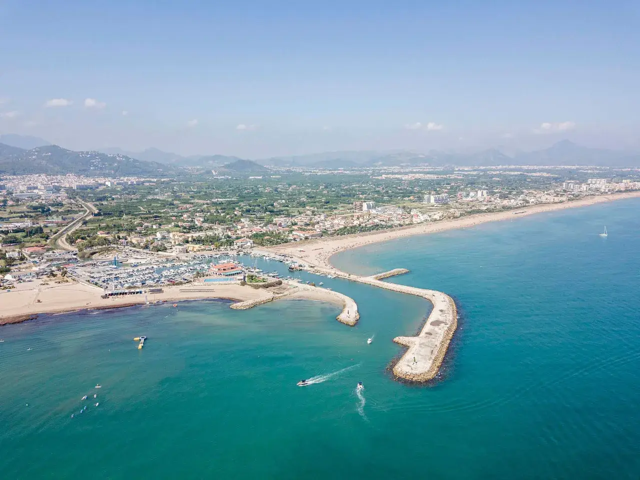Vista aérea de la playa de Oliva, con su puerto deportivo, arena dorada y aguas turquesas. Las opiniones sobre la playa de Oliva son muy positivas.