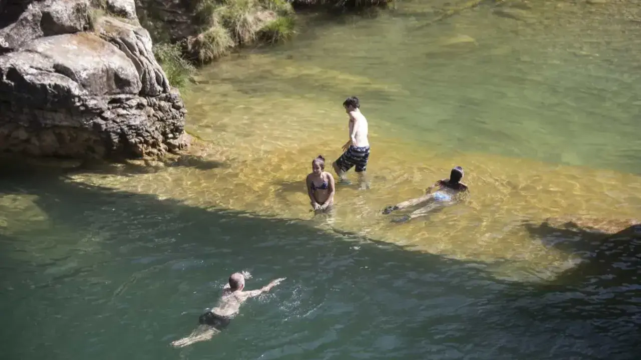 Gente disfrutando de un día en las playas cerca de Zaragoza, nadando y refrescándose en aguas cristalinas.