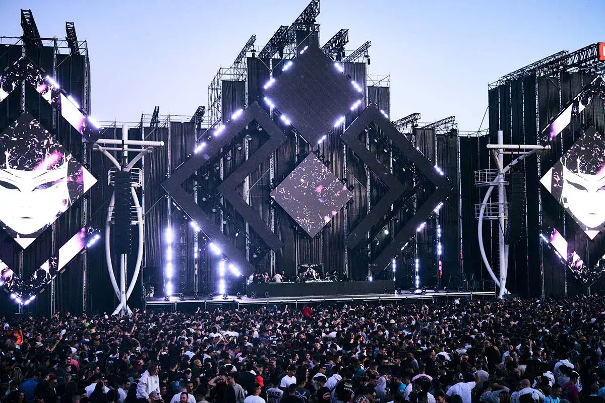 Multitud vibrante en un festival de música, escenario futurista con luces y pantallas. Una escena épica para tu summer story 2026.
