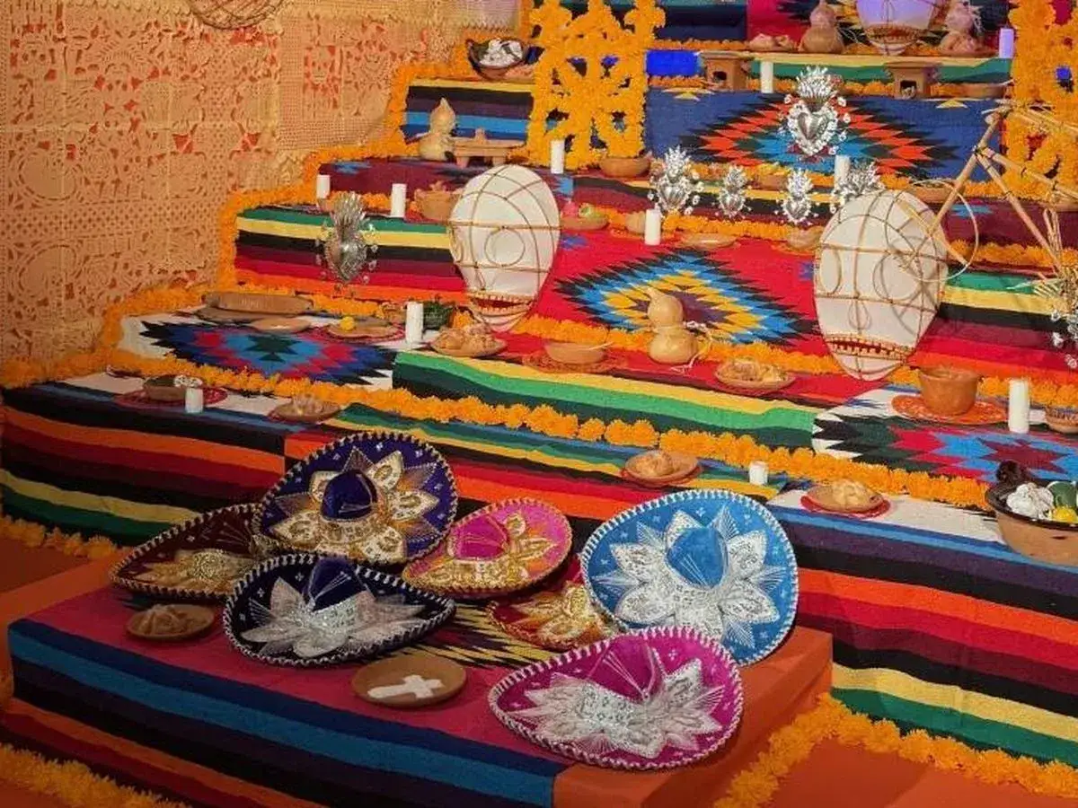 Un vibrante altar de los muertos en una casa de M&eacute;xico, adornado con sombreros, flores de cempas&uacute;chil y ofrendas.