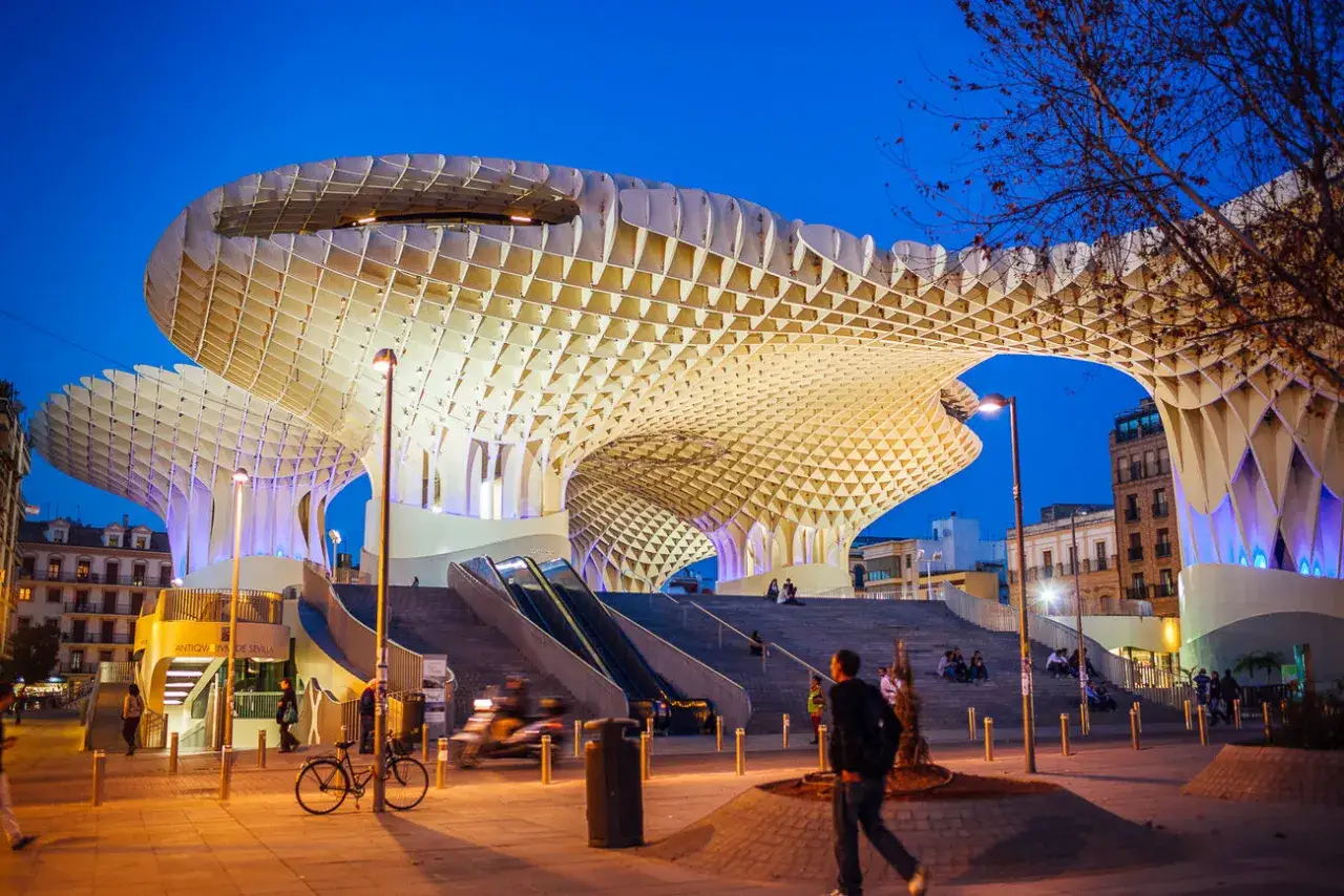 Las estatuas en Sevilla no son lo &uacute;nico impresionante. La arquitectura moderna de Las Setas ilumina la noche, con gente paseando y disfrutando.