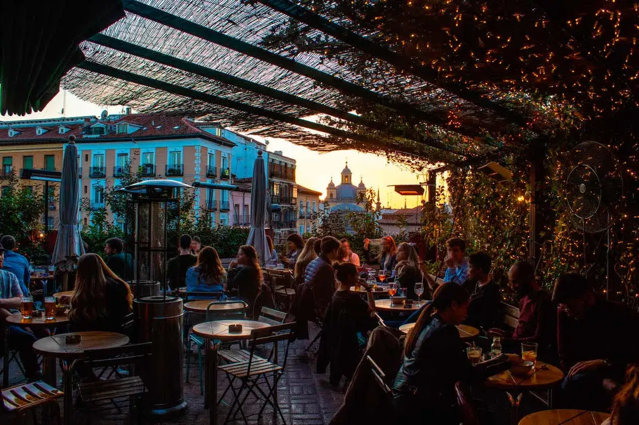 Gente disfrutando en una terraza de Madrid al atardecer, con luces cálidas y vistas a edificios históricos. Un lugar perfecto para el viajero en Madrid.