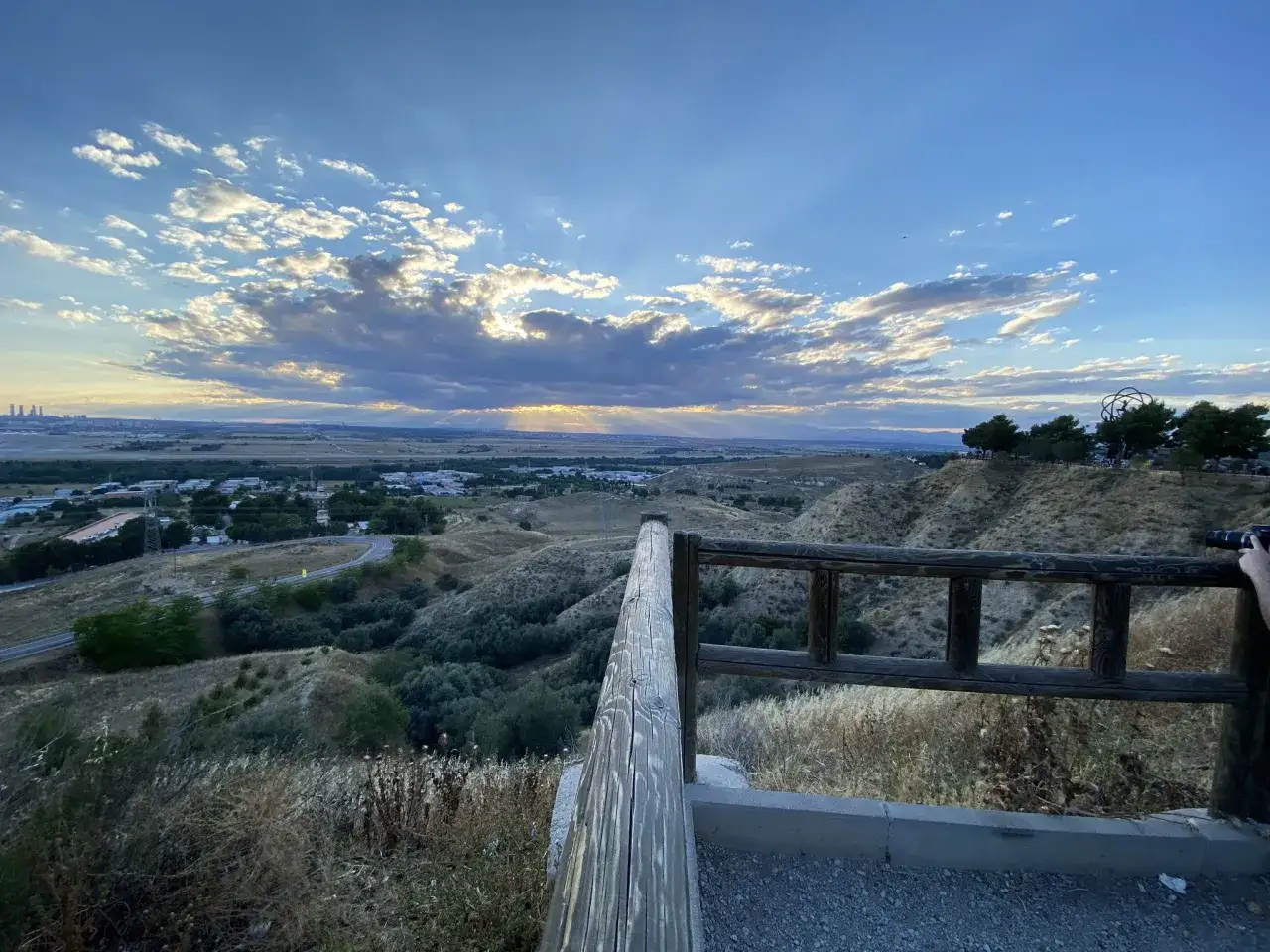 Atardecer en el mirador de Paracuellos, con rayos de sol atravesando las nubes y vistas a un valle verde y la ciudad a lo lejos.