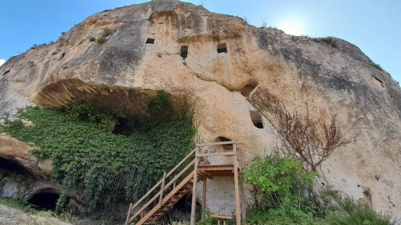 Antiguas cuevas y ventanas talladas en la roca de la Serra de Mariola, cubiertas de vegetación y con una escalera de madera.