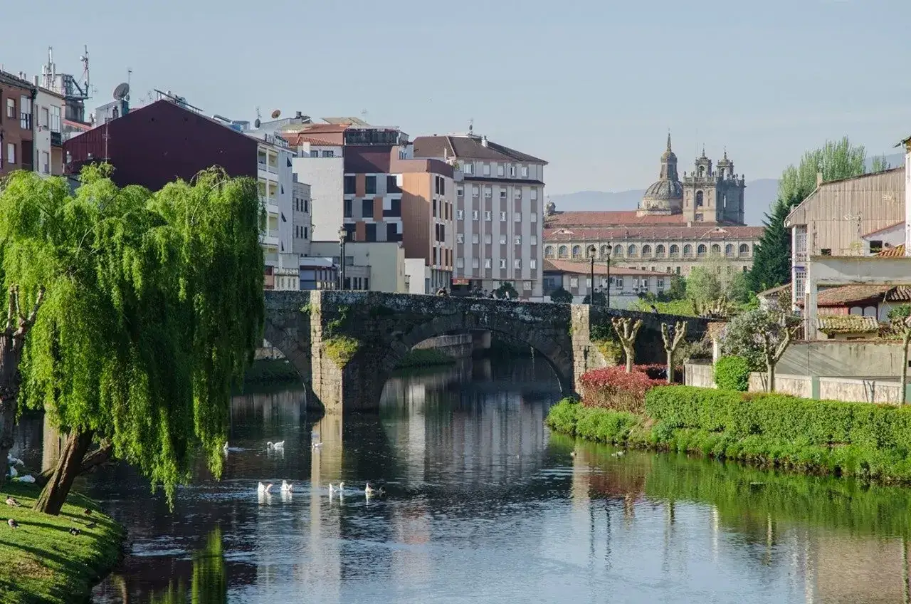 Un río tranquilo atraviesa un pueblo con un puente de piedra y edificios históricos. Un lugar encantador, como otros pueblos bonitos cerca de Monforte de Lemos.
