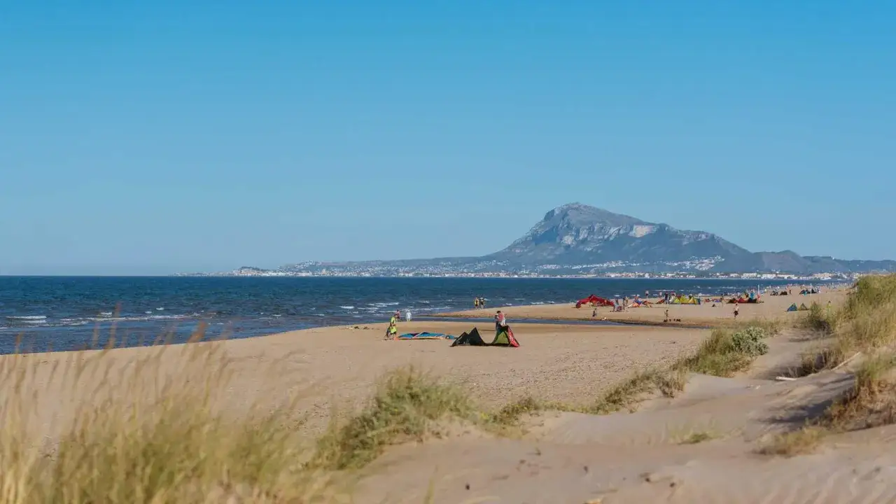 Gente disfrutando de la playa de Oliva, con kitesurfistas y tiendas en la arena. Monta&ntilde;a al fondo. Opiniones positivas para este destino.