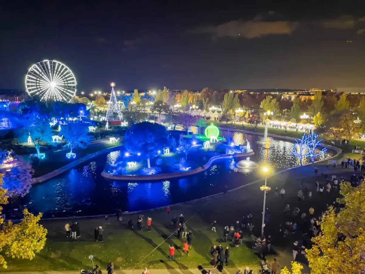 Vista nocturna de la ciudad de la Navidad en Madrid, con noria, &aacute;rbol iluminado, luces azules y gente paseando.