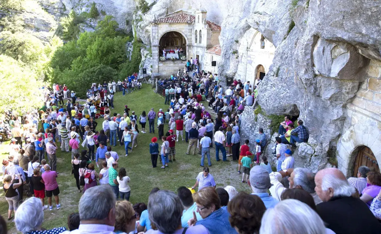 Multitud reunida en un evento religioso al aire libre, con una iglesia rupestre al fondo. Celebraci&oacute;n de fiestas en El Escorial.
