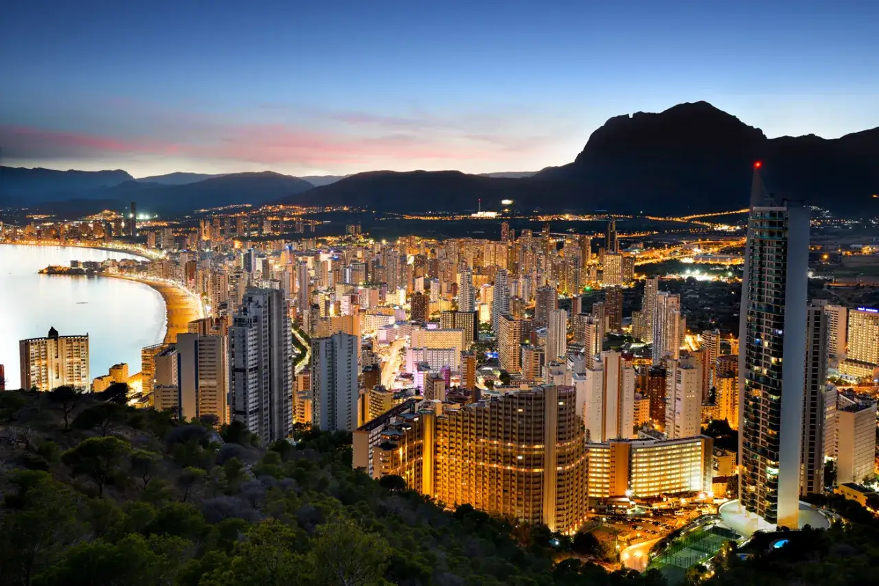 Vista nocturna desde un mirador de Benidorm, con la ciudad iluminada, la playa y el mar.