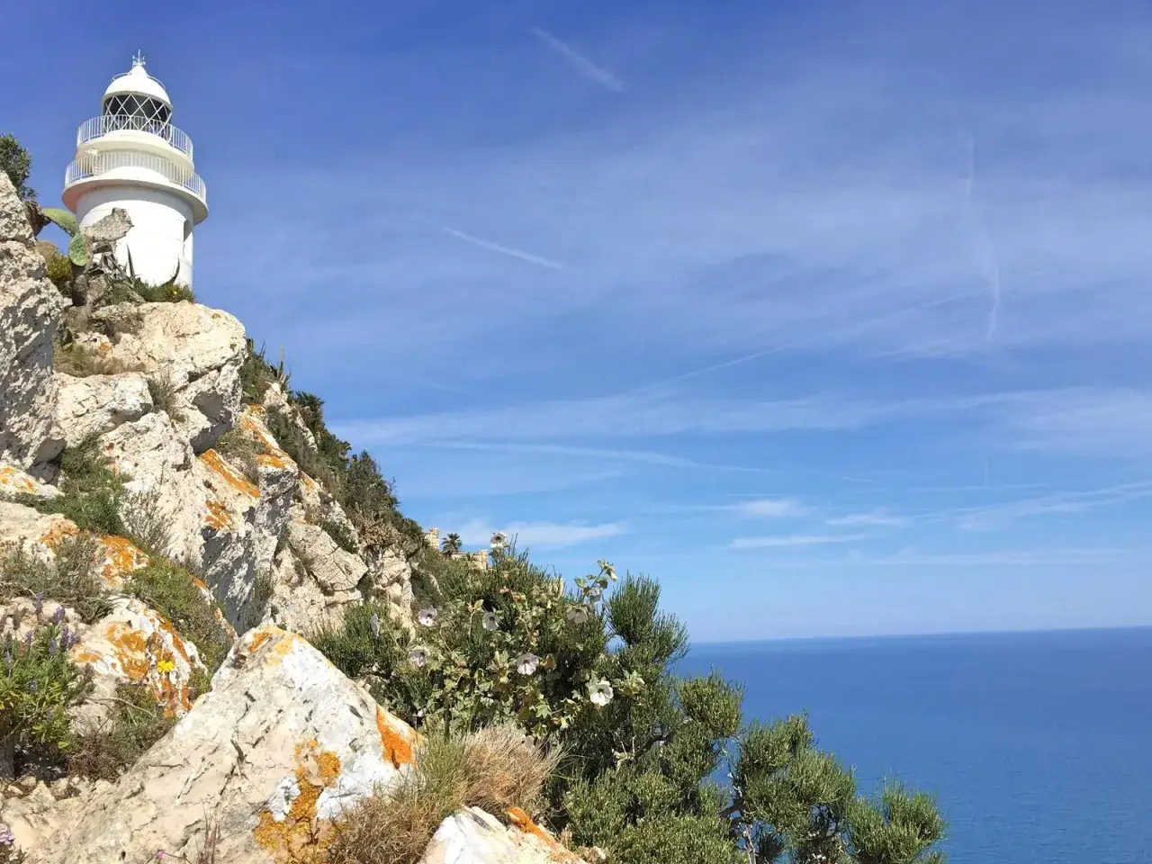 El faro del Cabo de San Antonio se alza sobre rocas escarpadas, vigilando el azul intenso del mar Mediterráneo bajo un cielo despejado.