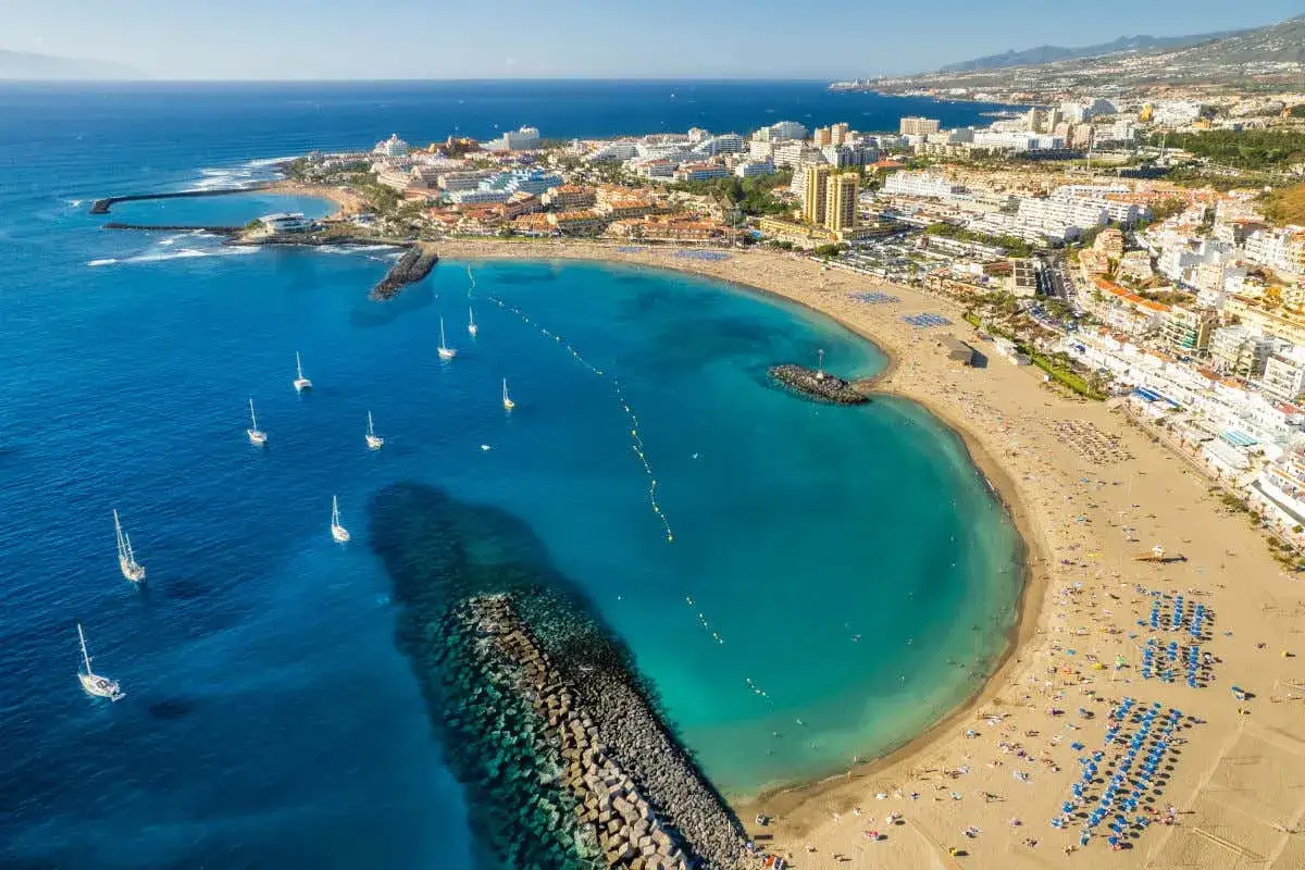 Vista aérea de la playa de los gigantes con aguas turquesas, veleros y una ciudad costera al fondo.
