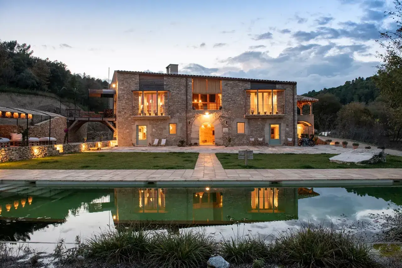 El restaurante El Castell de Brunyola, una masía de piedra iluminada al atardecer, con piscina reflejando sus luces y rodeada de naturaleza.