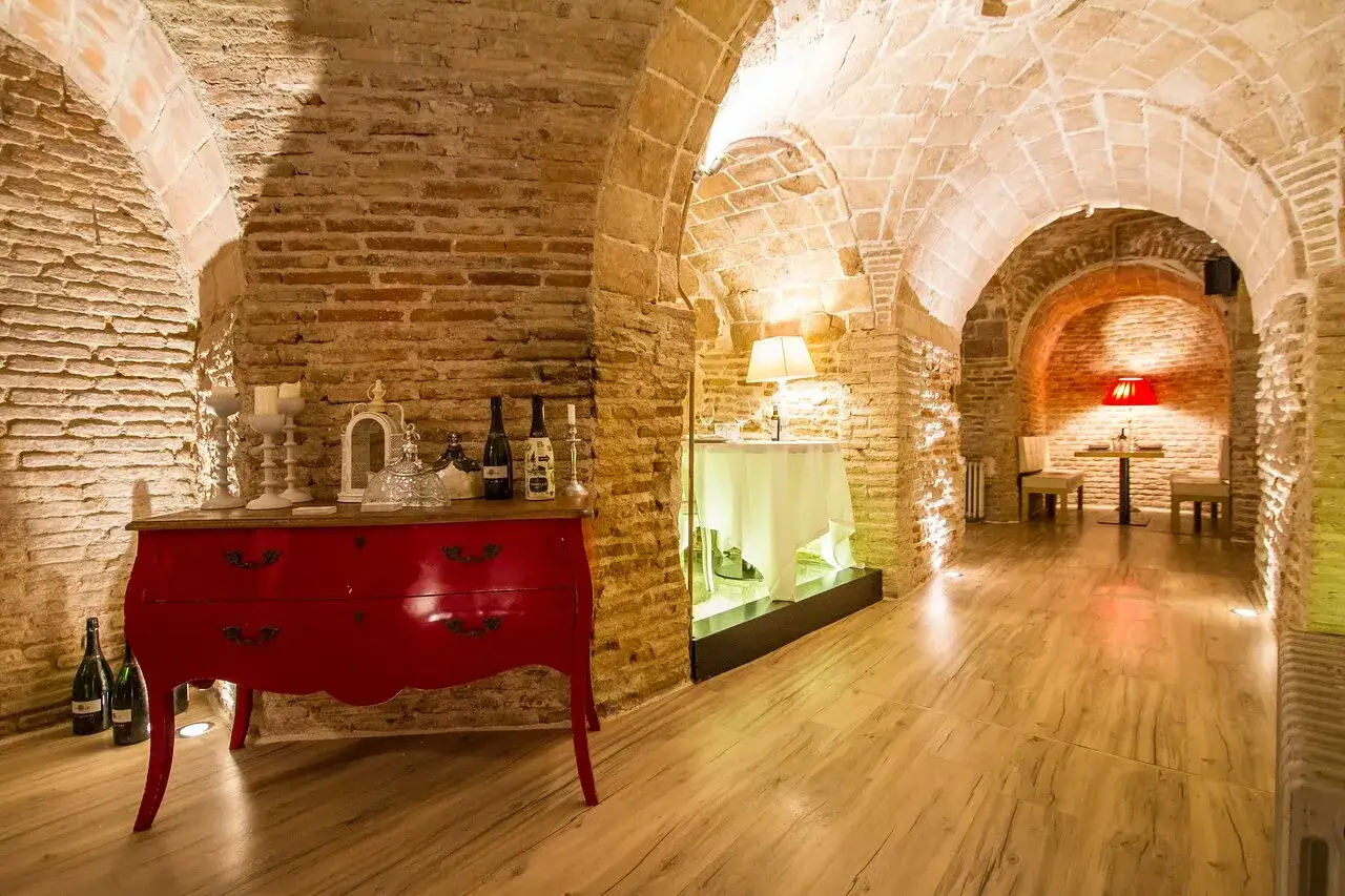 Bodega con arcos de ladrillo, c&oacute;moda roja, botellas de vino y mesas dispuestas para una cena &iacute;ntima. Aqu&iacute; se guardan las opiniones de bodega de los secretos.