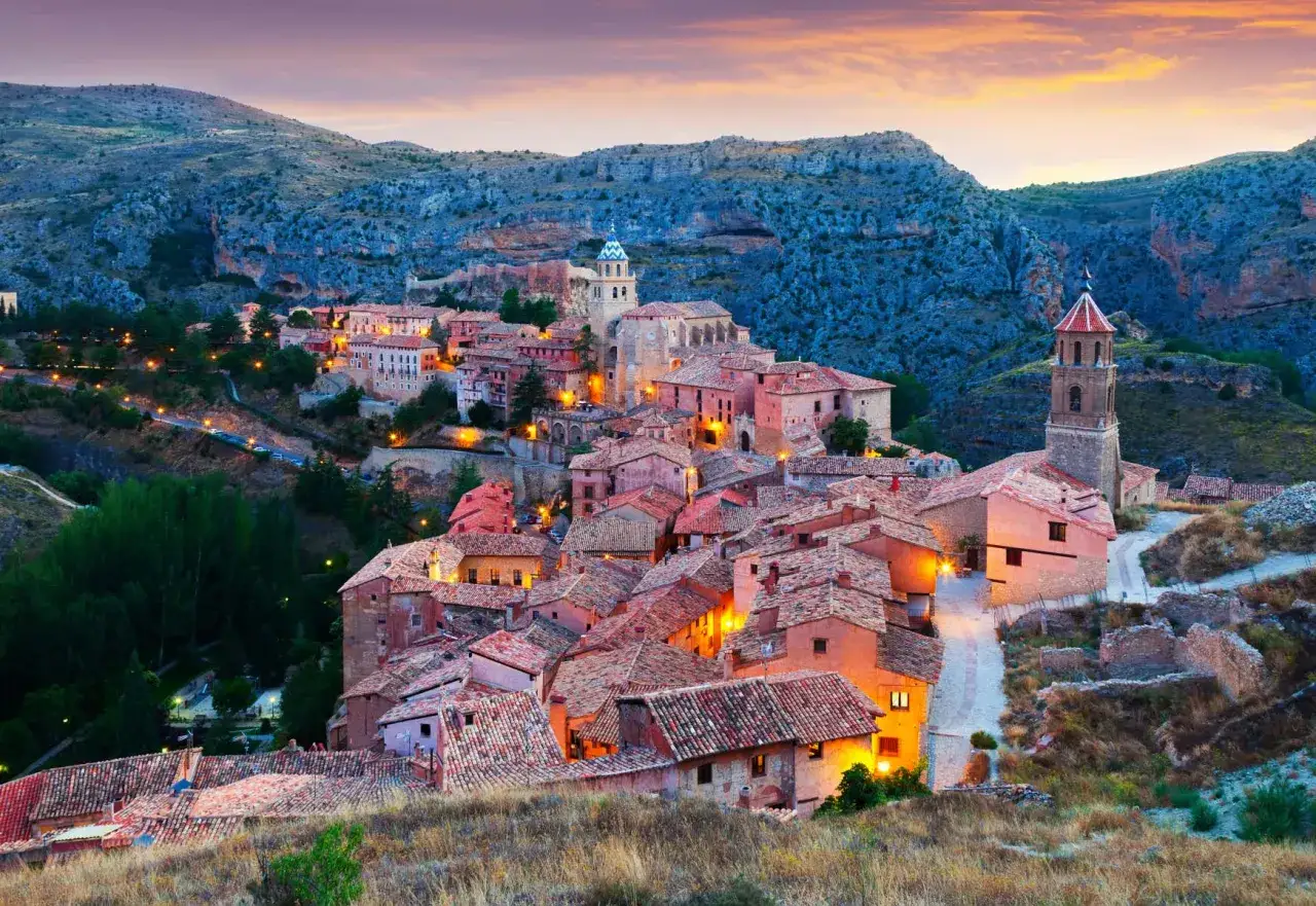 Pueblo medieval iluminado al atardecer, con tejados rojos y torres, uno de los pueblos m&aacute;s bonitos de Teruel.