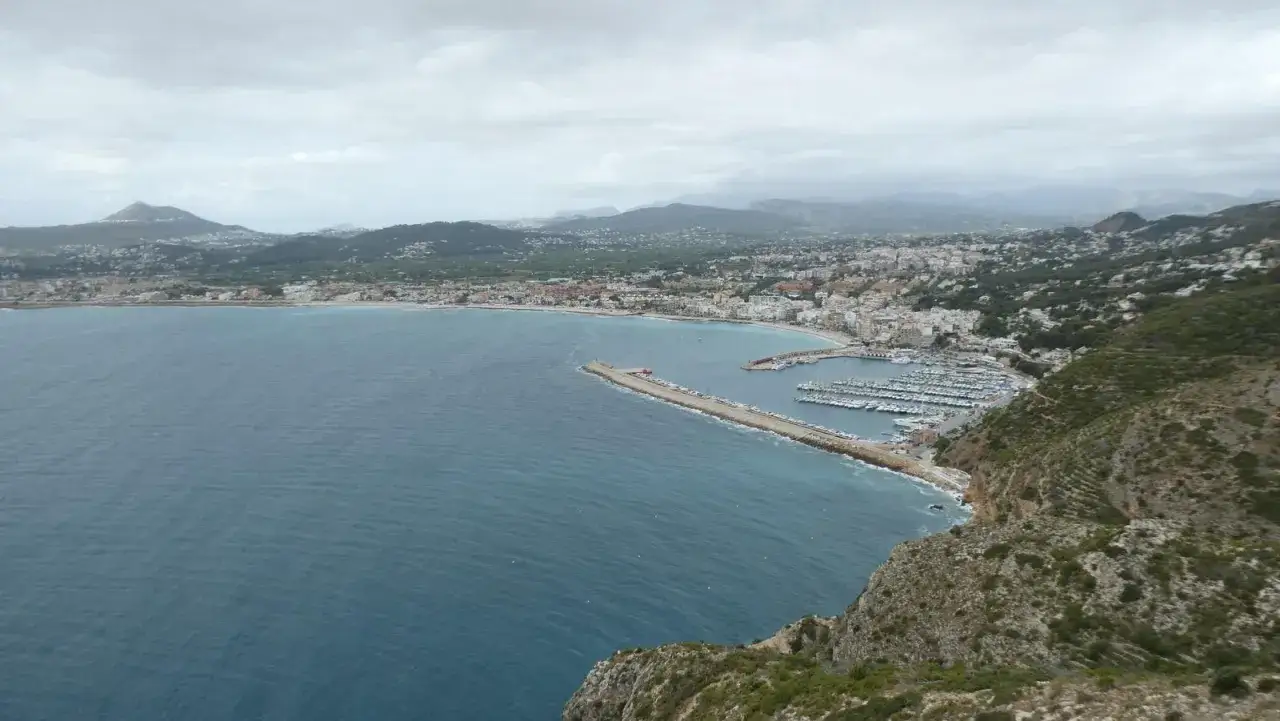 Vista panorámica de la bahía con el faro del Cabo de San Antonio, un puerto deportivo y la ciudad costera.