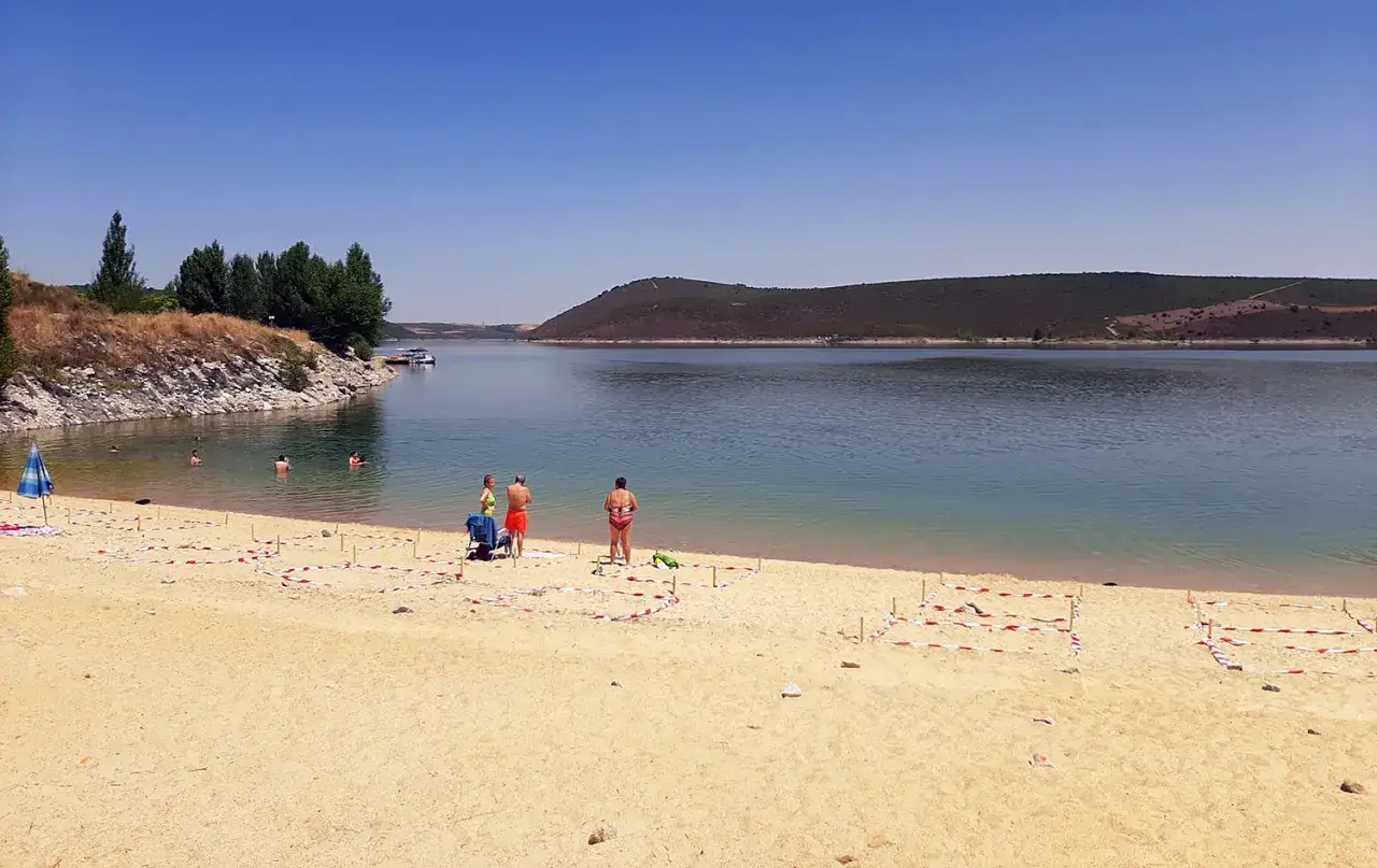 Gente disfrutando del sol y el agua en la playa fluvial de Ricobayo. El agua tranquila invita a un refrescante baño.