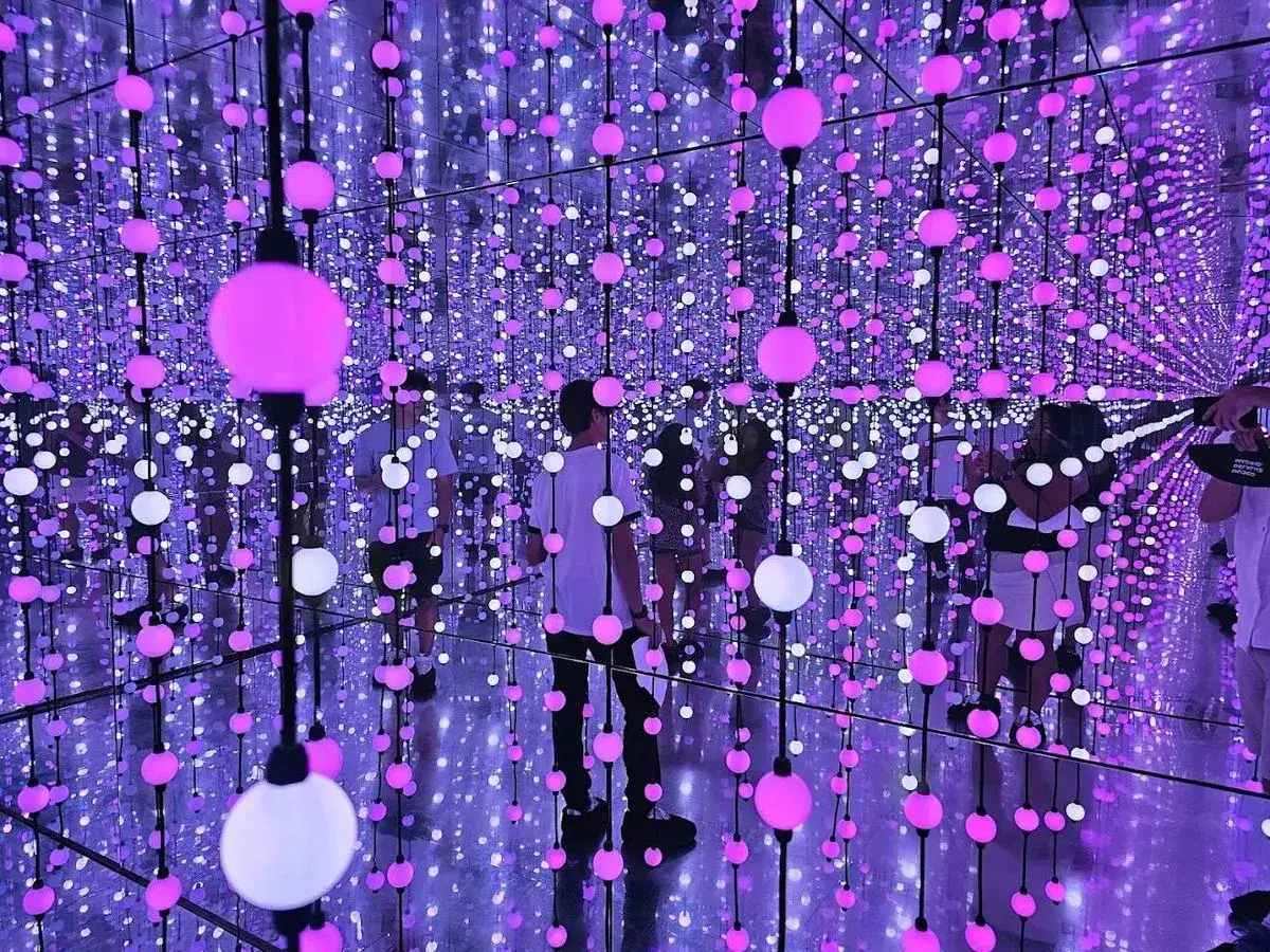 Gente explorando un nomad museo inmersivo lleno de luces colgantes rosas y blancas, creando un efecto infinito.