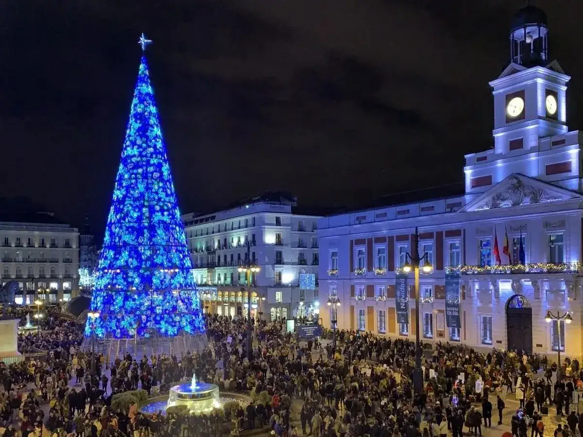 Una multitud celebra la Navidad en la Puerta del Sol de Madrid, bajo un &aacute;rbol gigante iluminado de azul. &iexcl;Excelentes planes de Navidad en Madrid!