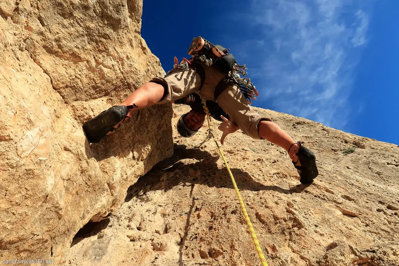 Escalada en Alicante: un escalador sonríe mientras se aferra a una pared rocosa bajo un cielo azul brillante.