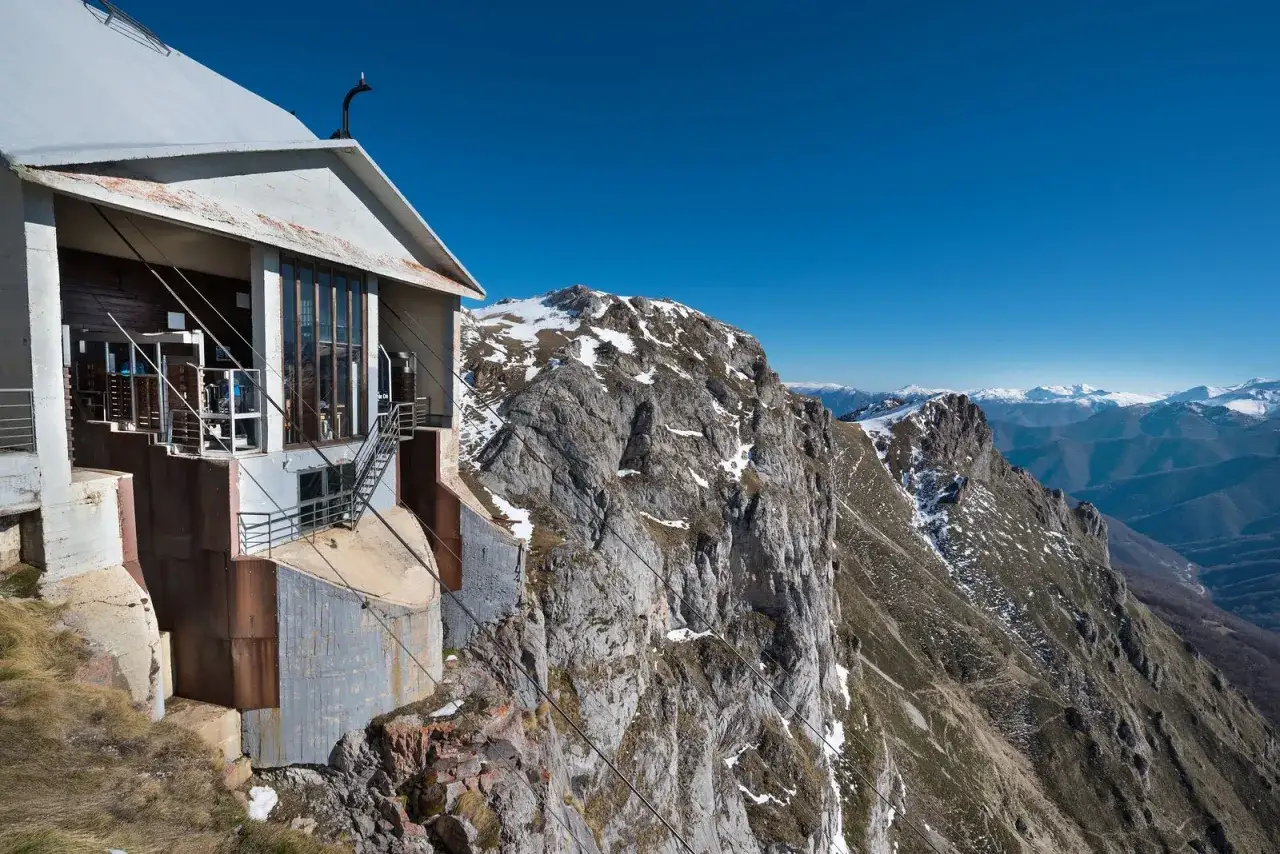 Edificio de montaña con vistas a los Picos de Europa en Cantabria. El sol brilla sobre las cumbres nevadas.