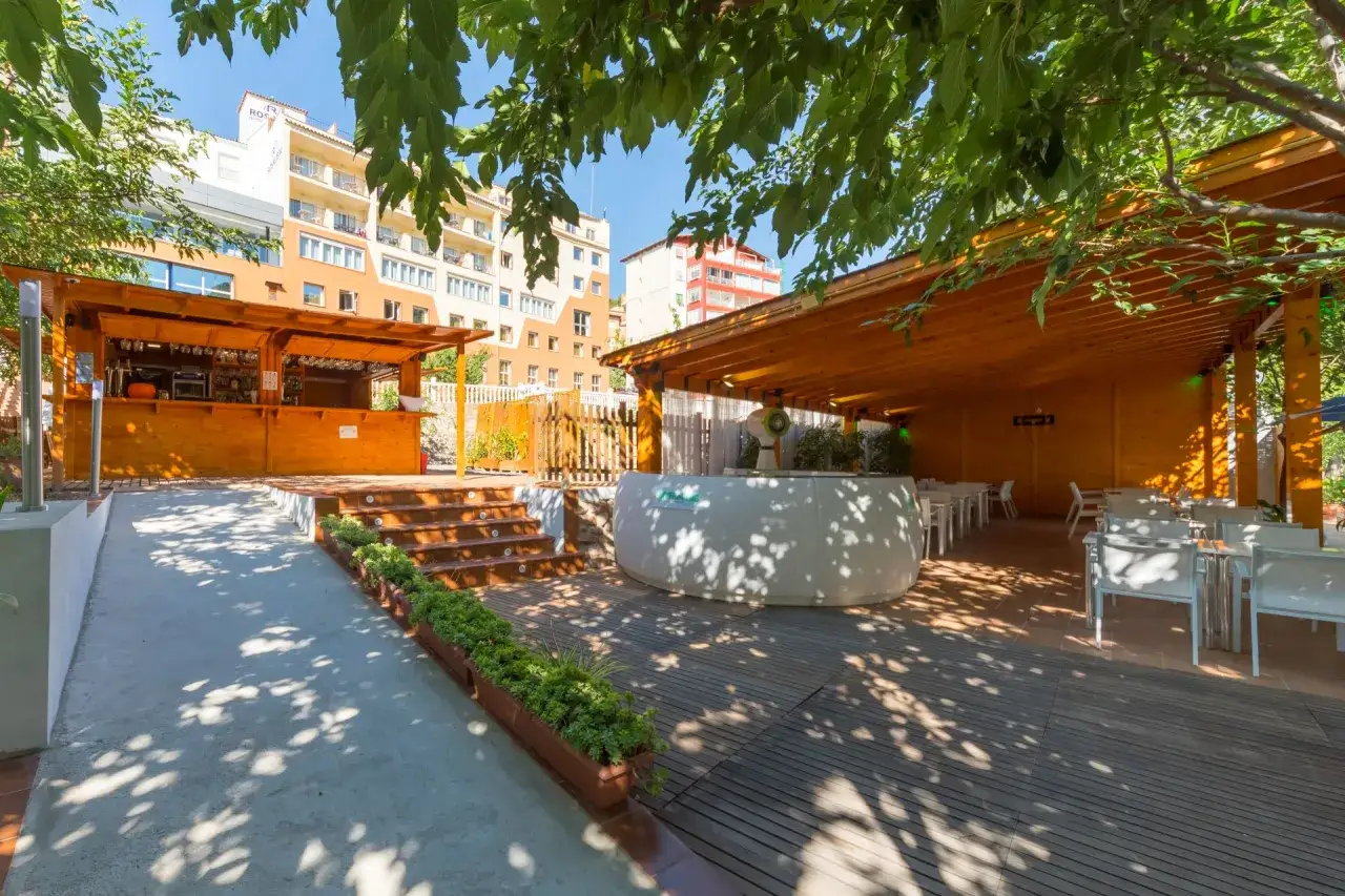 Terraza de madera con bar y mesas, ideal para saber donde comer en Montanejos. Edificios al fondo.