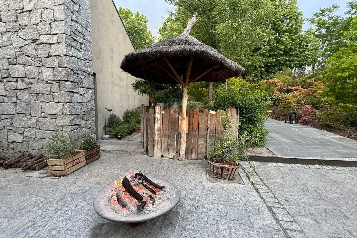 Acogedor rinc&oacute;n en fotos de restaurante Filand&oacute;n: hoguera encendida, sombrilla de paja y jard&iacute;n exuberante.