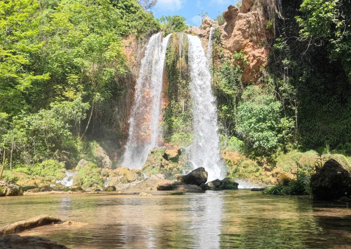 Cascada imponente cayendo en el lago de Anna, rodeada de vegetación exuberante y rocas.