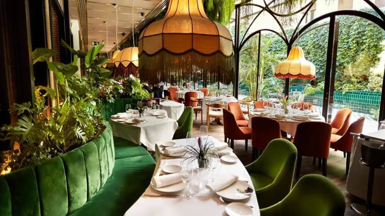 Mesas elegantemente puestas en un restaurante con exuberante vegetación, evocando la atmósfera de las opiniones de restaurante amazónico.