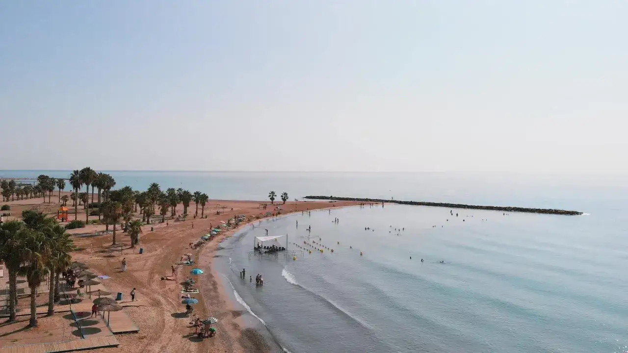 Vista aérea de la playa de Chilches, con palmeras, sombrillas y gente disfrutando del mar. Las opiniones sobre la playa de Chilches son muy positivas.