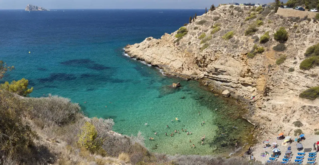 La cala Tío Ximo, con sus aguas cristalinas y rocas escarpadas, invita a un refrescante baño entre bañistas y el sol.