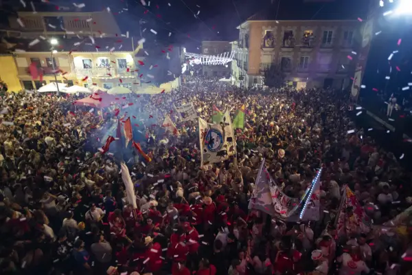 Multitud celebrando con confeti y banderas en una calle por la noche.