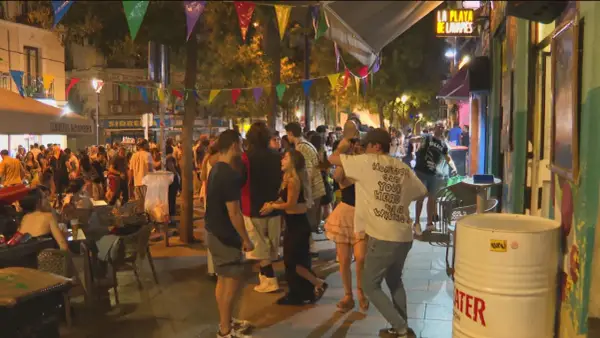 Gente disfrutando de las fiestas de San Lorenzo en Madrid, con luces, música y ambiente festivo en la calle.